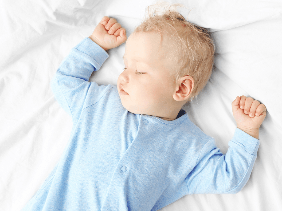 Baby asleep on their back on white bedding with arms relaxed above their head