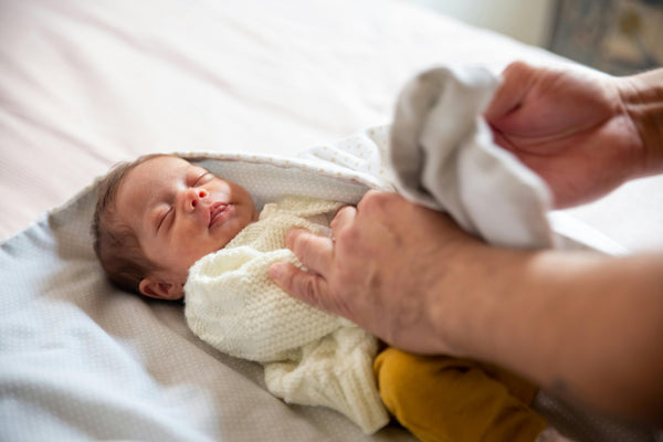 A parent dressing a newborn in a knitted cardigan on a changing mat, choosing layers for sleep