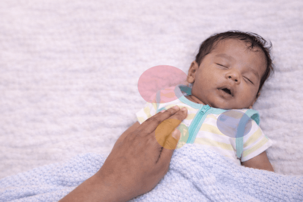A parent's hand resting on a sleeping baby's chest to check whether they are too warm or too cold