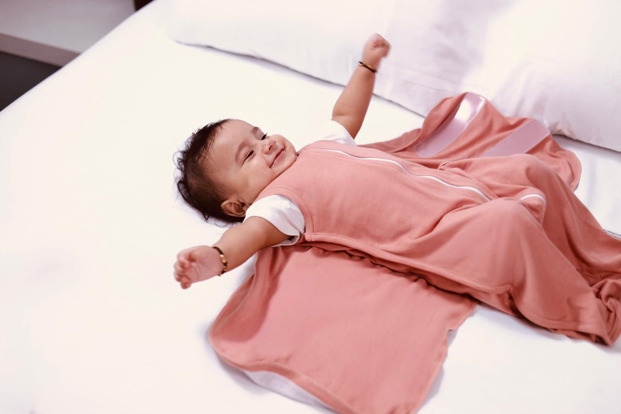 Baby lying on a white surface wearing a clay nest peach outfit with white trim.