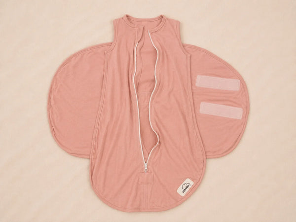 A dusty pink baby sleep sack with a front zipper, white drawstring, and two elasticated leg openings, laid flat on a light beige background.