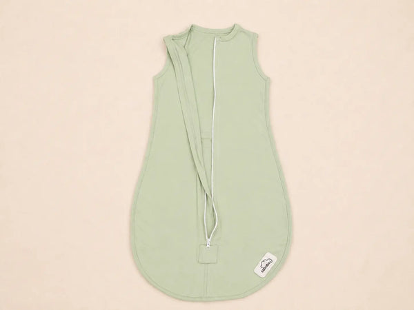A sage green baby sleep sack with a white zipper and drawstring closure, laid flat on a light beige background.