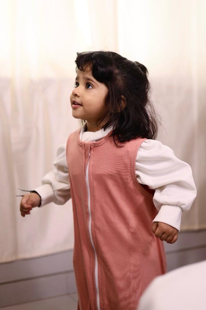 Child wearing a clay nest peach outfit with a white shirt underneath, standing against a neutral background.