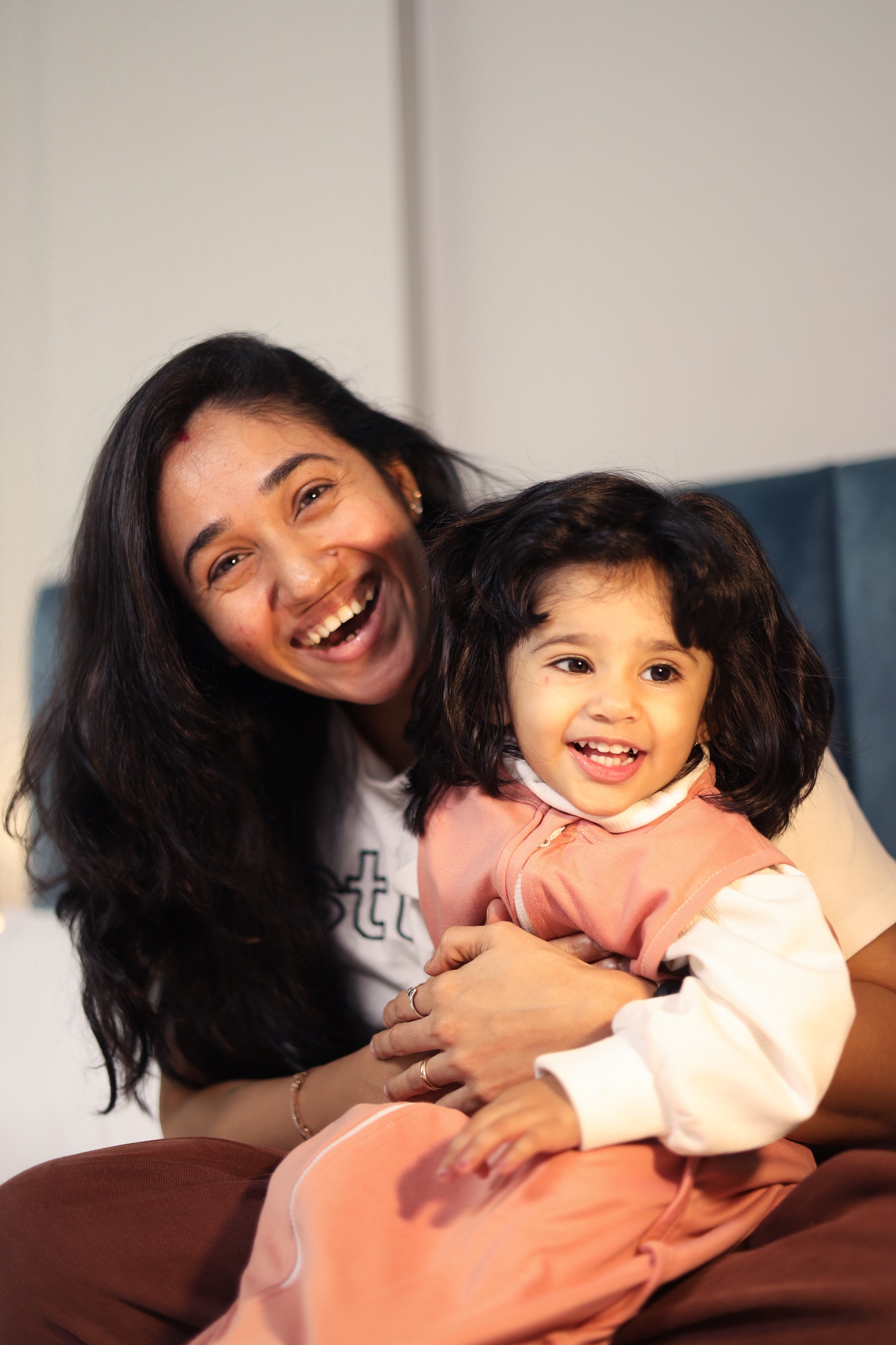 Woman holding a child and smiling, with a plain background