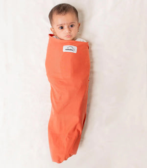 Baby wrapped in an orange swaddle with a visible brand label on a white background