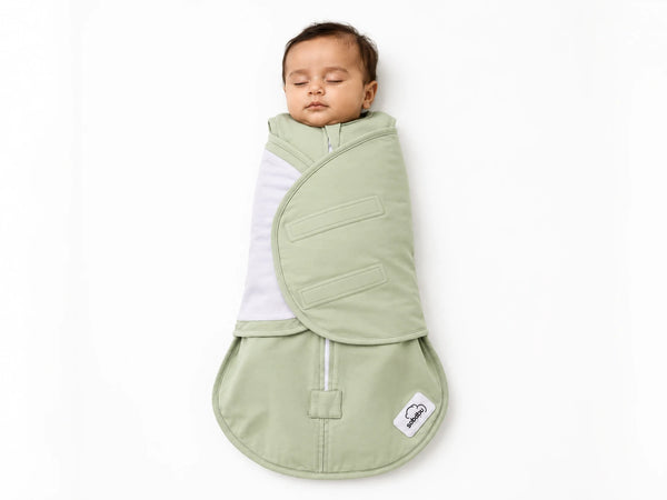 A sleeping baby swaddled in a sage green wrap blanket with a white inner layer, shown against a plain white background. The brand label 'Bebamour' is visible on the bottom right corner of the blanket.
